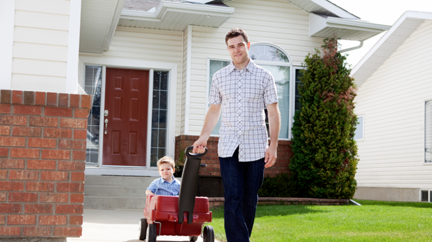 Child in red wagon being pulled by father in front of house
