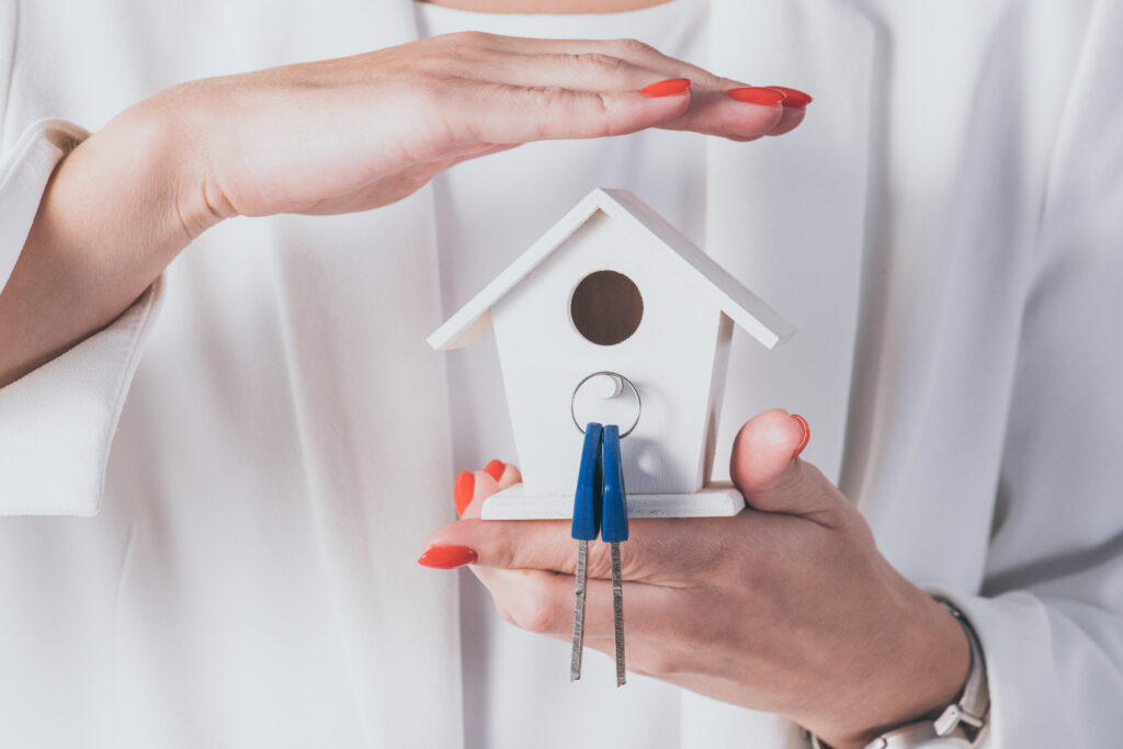 A business woman shielding a small birdhouse with house keys in it